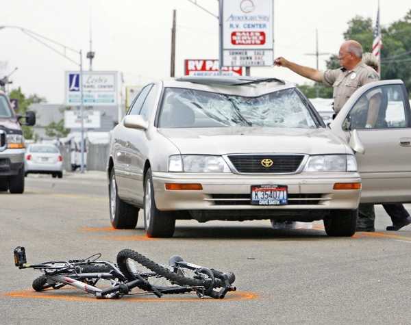 A destroyed bicycle on the ground with a car, the windshield and roof broken by the impact of the rider's body.