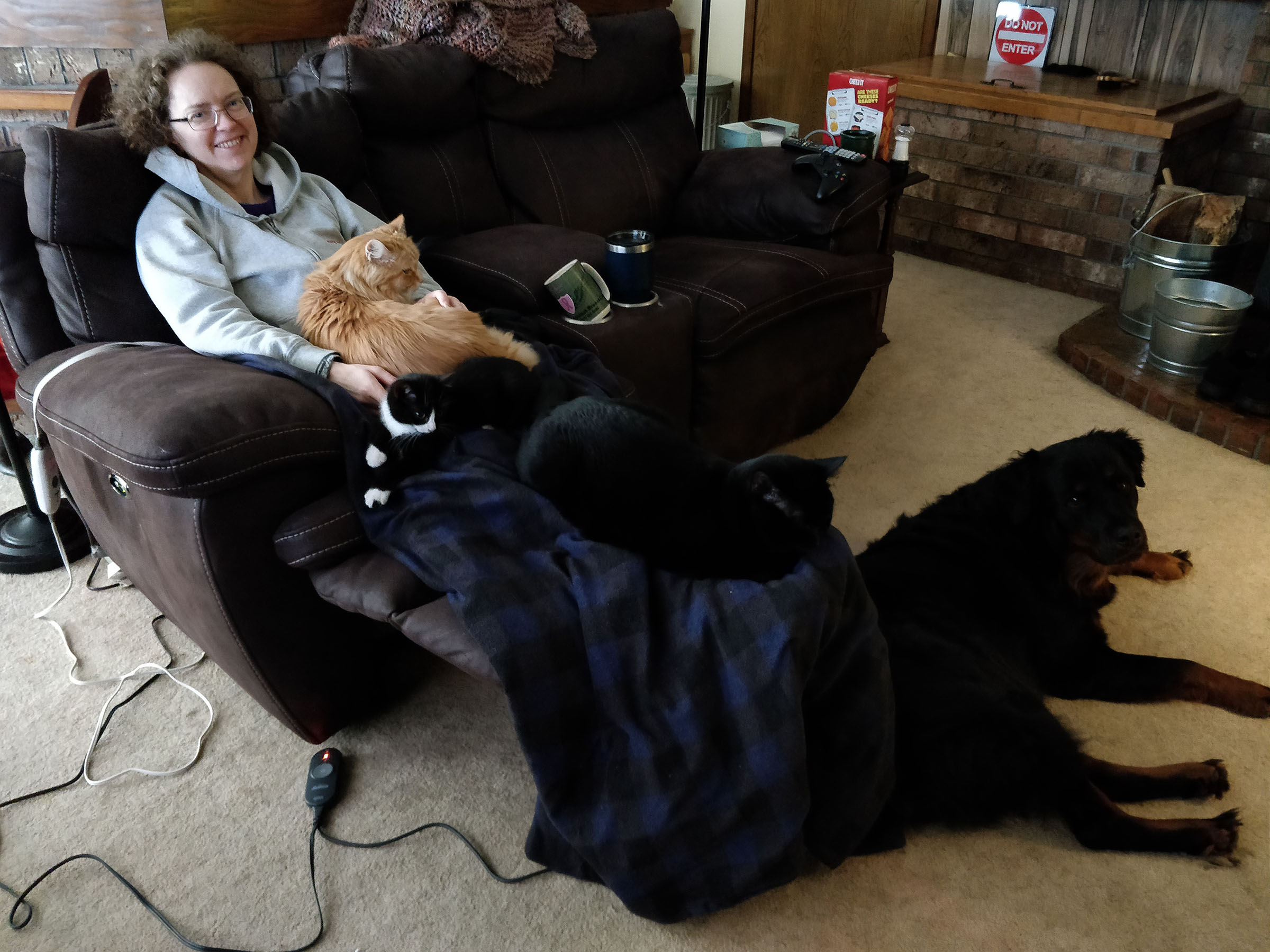 Heather on couch with coffee, three cats, and one huge dog.