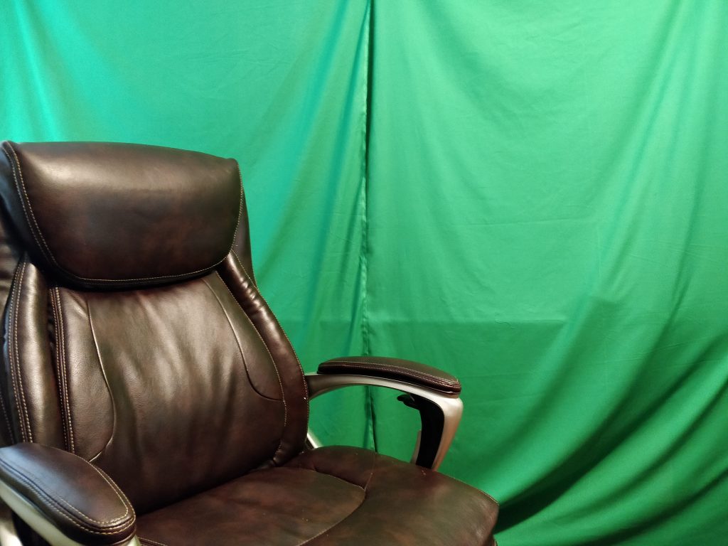 An empty leather office chair in front of green fabric, hanging like curtains.