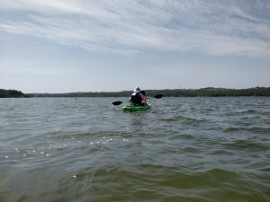 Woman kayaking on a slightly choppy lake, facing away from the camera.