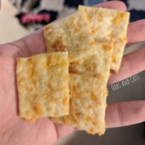 Freshly baked cheese crackers, made with sourdough, in a man's hand. There are big crystals of salt on the crackers, and there's an Orks and Cats watermark.