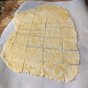 Cracker dough, brushed with oil and cut into squares for baking, resting on a piece of parchment paper.