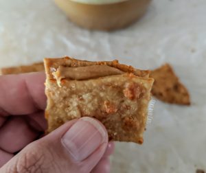 Two cheddar cheese sourdough crackers with a layer of peanut butter sandwiched between them, held in a man's hand.